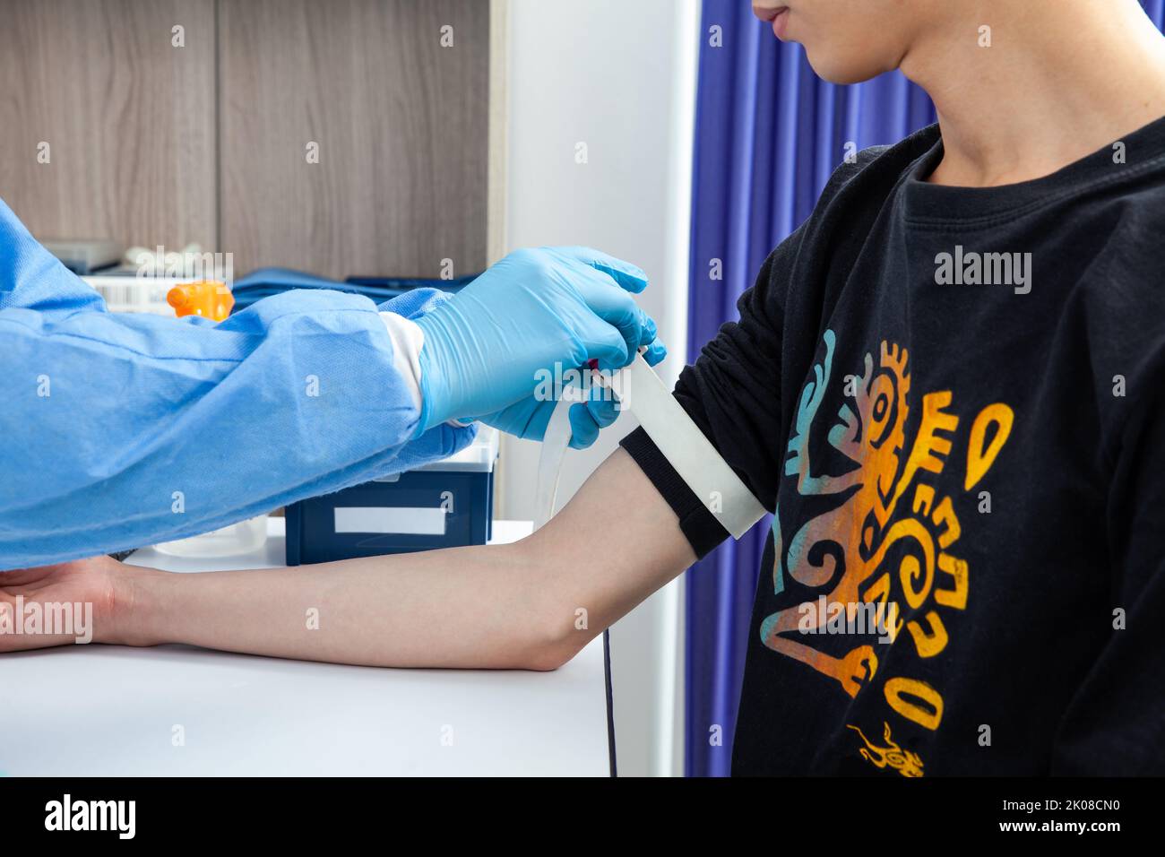 Nurse tightening the elastic band on a male patient arm to collect a blood sample from in a clinic Stock Photo
