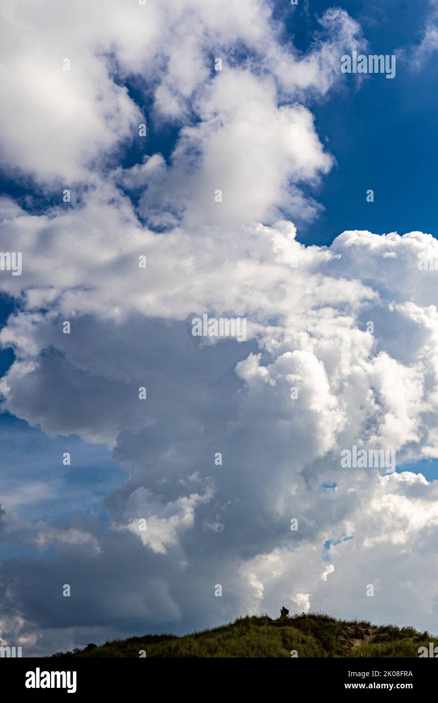 Portrait format image of a landscape photographer looking tiny under a huge towering cumulus cloud Stock Photo