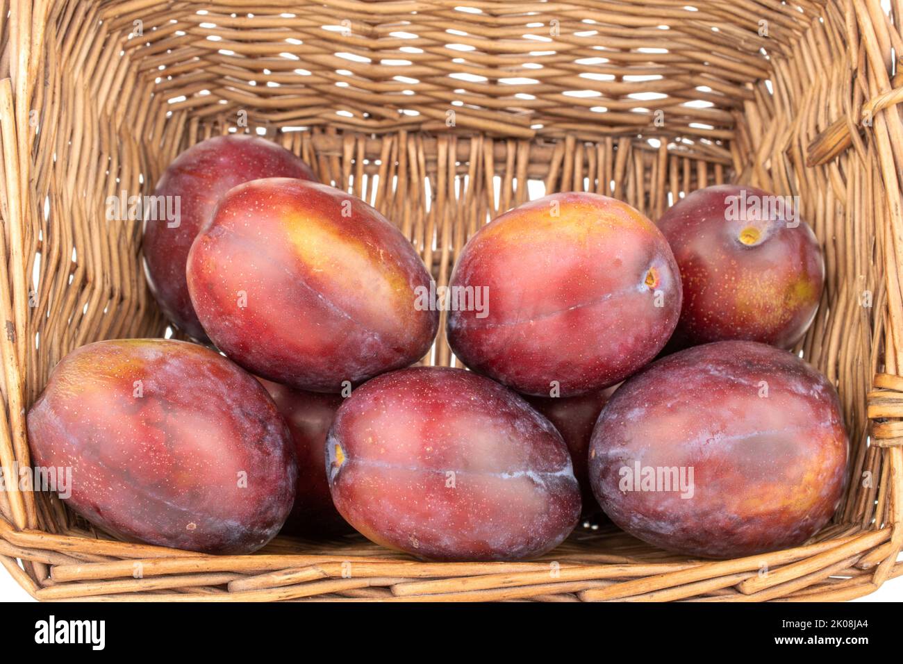 Several juicy plums in a vine basket, close-up, isolated on a white background. Stock Photo
