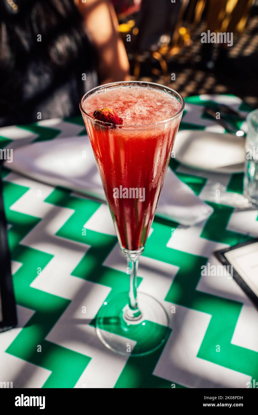 red, pink cocktail in champagne flute with rosebud garnish on green and white chevron stripe tablecloth at restaurant Stock Photo