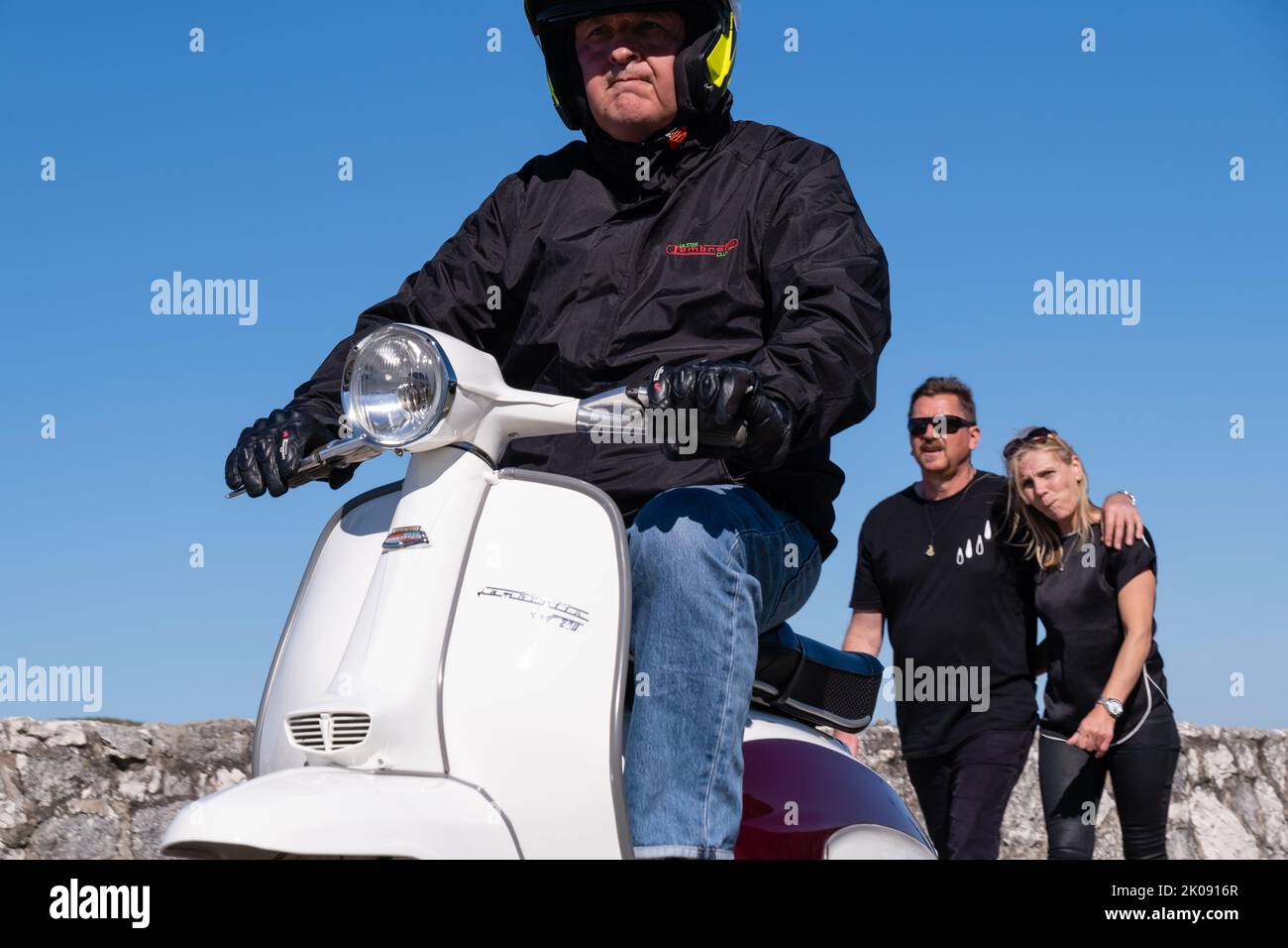 Man riding crisp white classic Lambretta scooter leaving scooter rally at harbour. Ballintoy, UK - September 10th 2022. Stock Photo