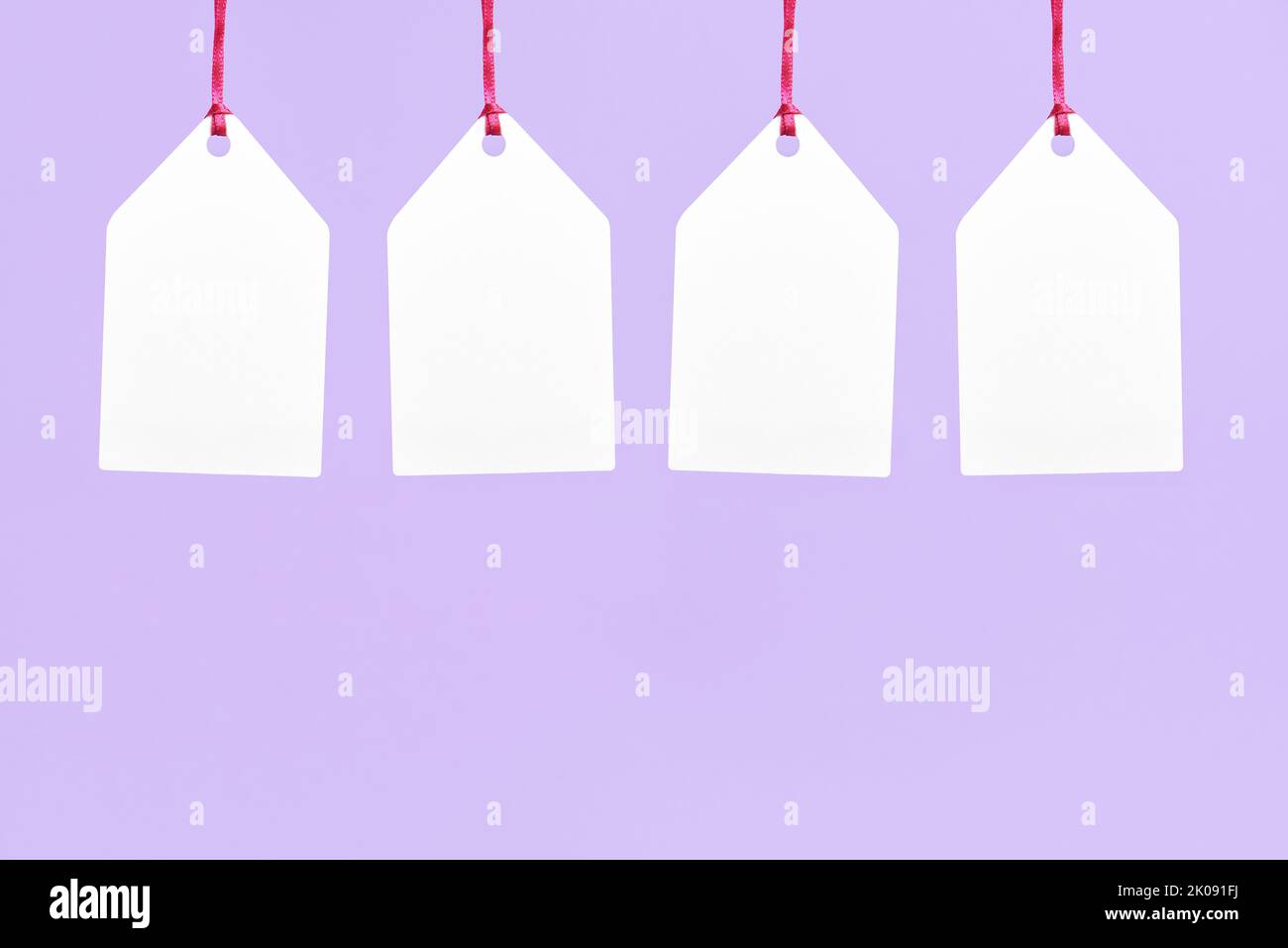 Four blank white paper labels hanging on a pastel lilac background. Simple design with copy space. Concepts: shopping, seasonal sales, black friday di Stock Photo