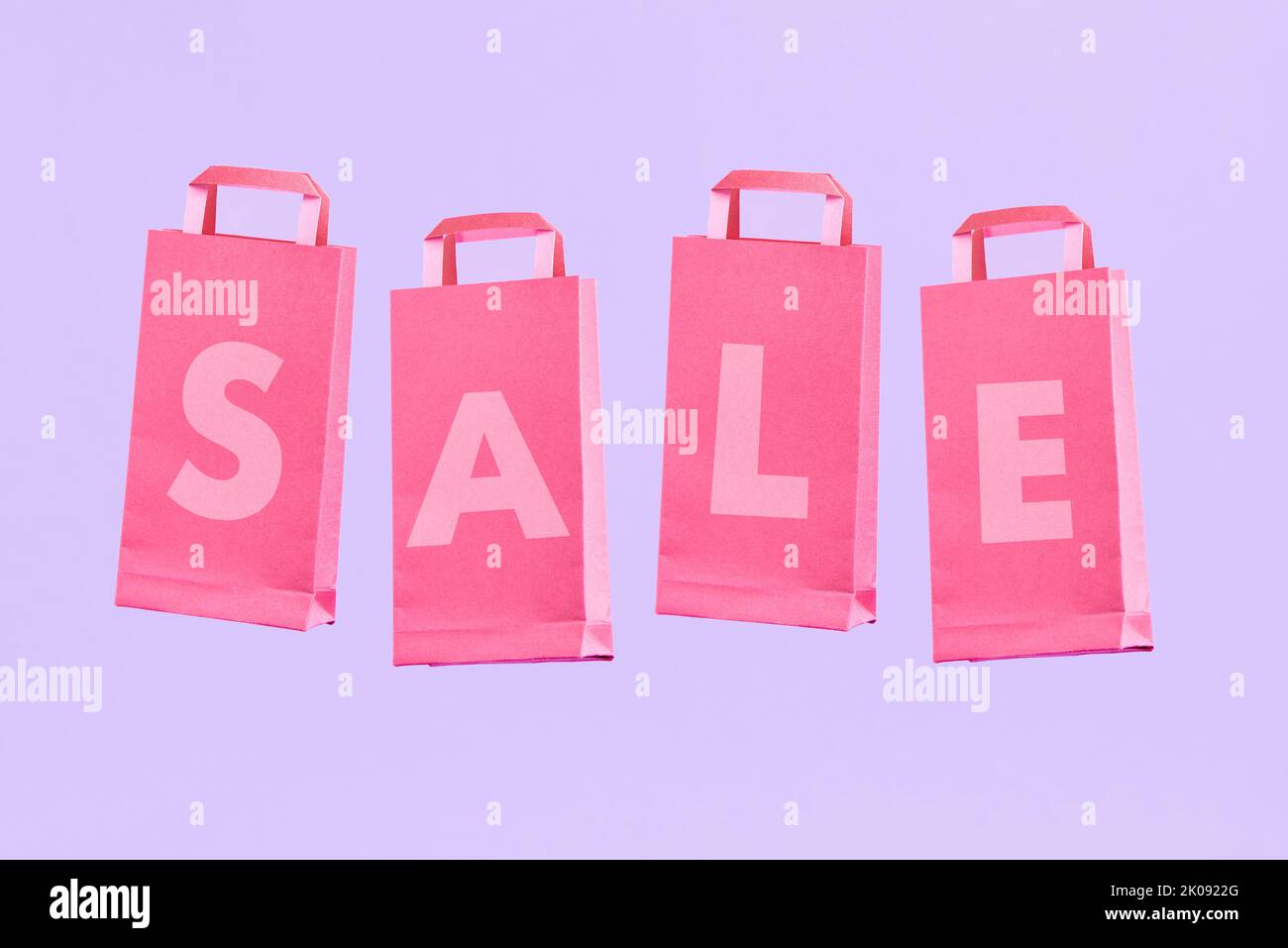 Word Sale written on a group of pink paper shopping bags, on a pastel lilac background. Minimalist trendy design with copy space. Stock Photo