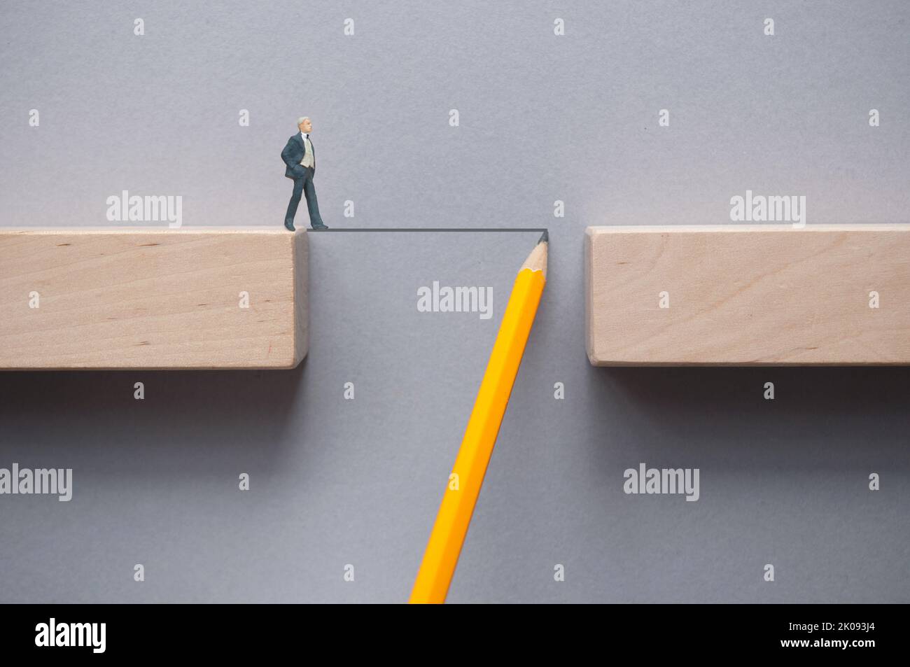 Miniature business man crossing a line sketched with a pencil bridging the gap between wooden blocks Stock Photo