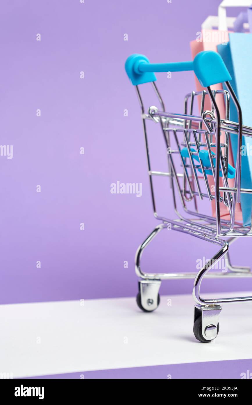 Shopping cart loaded with paper bags on a pastel lilac background. Vertical design with copy space. Concepts: market deals, seasonal sales and discoun Stock Photo