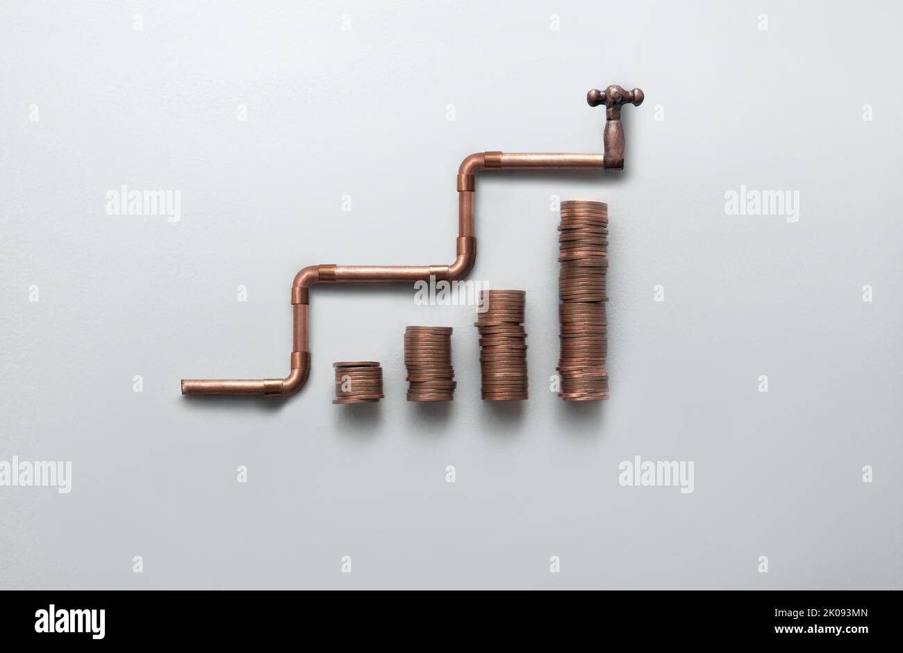 Copper piping with tap rising upwards alongside stacks of coins, increase in energy bills, costs and prices concept Stock Photo
