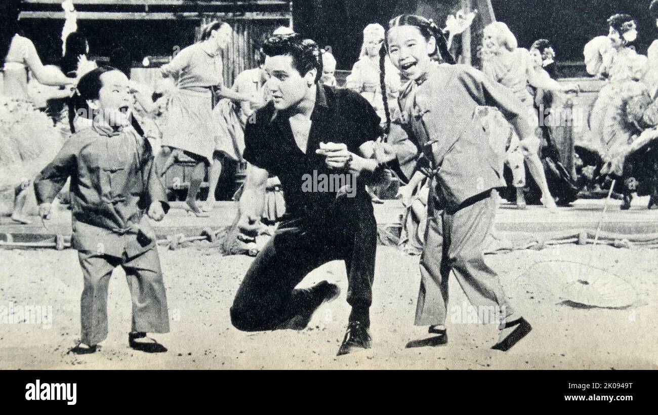 Newspaper review of Girls! Girls! Girls! 1962 film featuring Elvis Presley. Photograph of Elvis Presley with Ginny Tiu and Elizabeth Tiu. Stock Photo