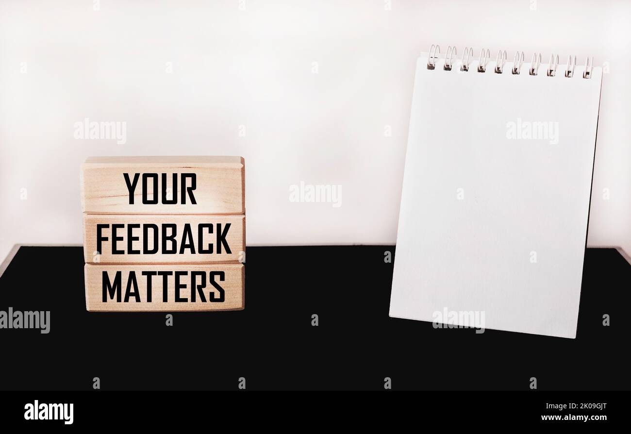 YOUR FEEDBACK MATTERS text on wooden blocks and white and black background with notepad for writing.Business concept Stock Photo