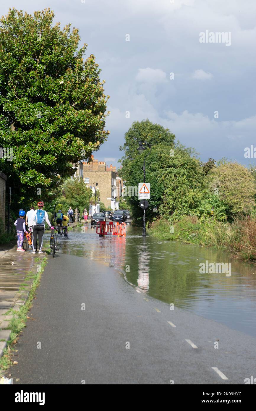 London, England, UK. 10th Sep 2022. Adults and kids ciclysts blocked on kerb wondering how to cross the road as water floods the Thames riverbank after recent thunderstorms. Cristina Massei/Alamy Live News Stock Photo