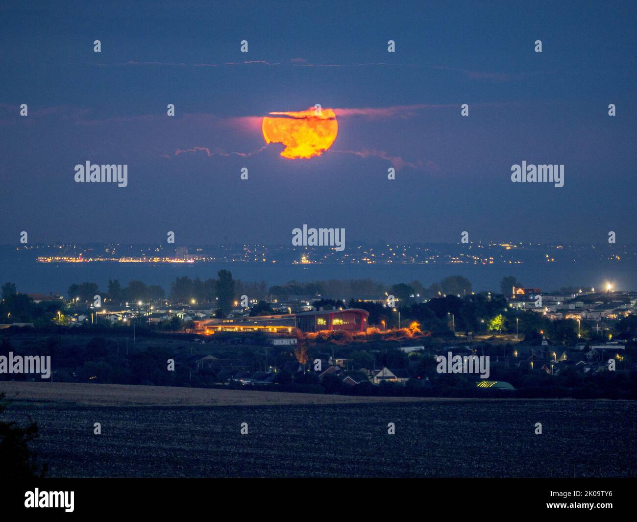 Eastchurch, Kent, UK. 10th Sep, 2022. UK Weather: the full Harvest Moon seen rising and peeking through a gap in cloud cover over Leysdown and the Kent coast this evening - pictured from Eastchurch, Kent. Credit: James Bell/Alamy Live News Stock Photo