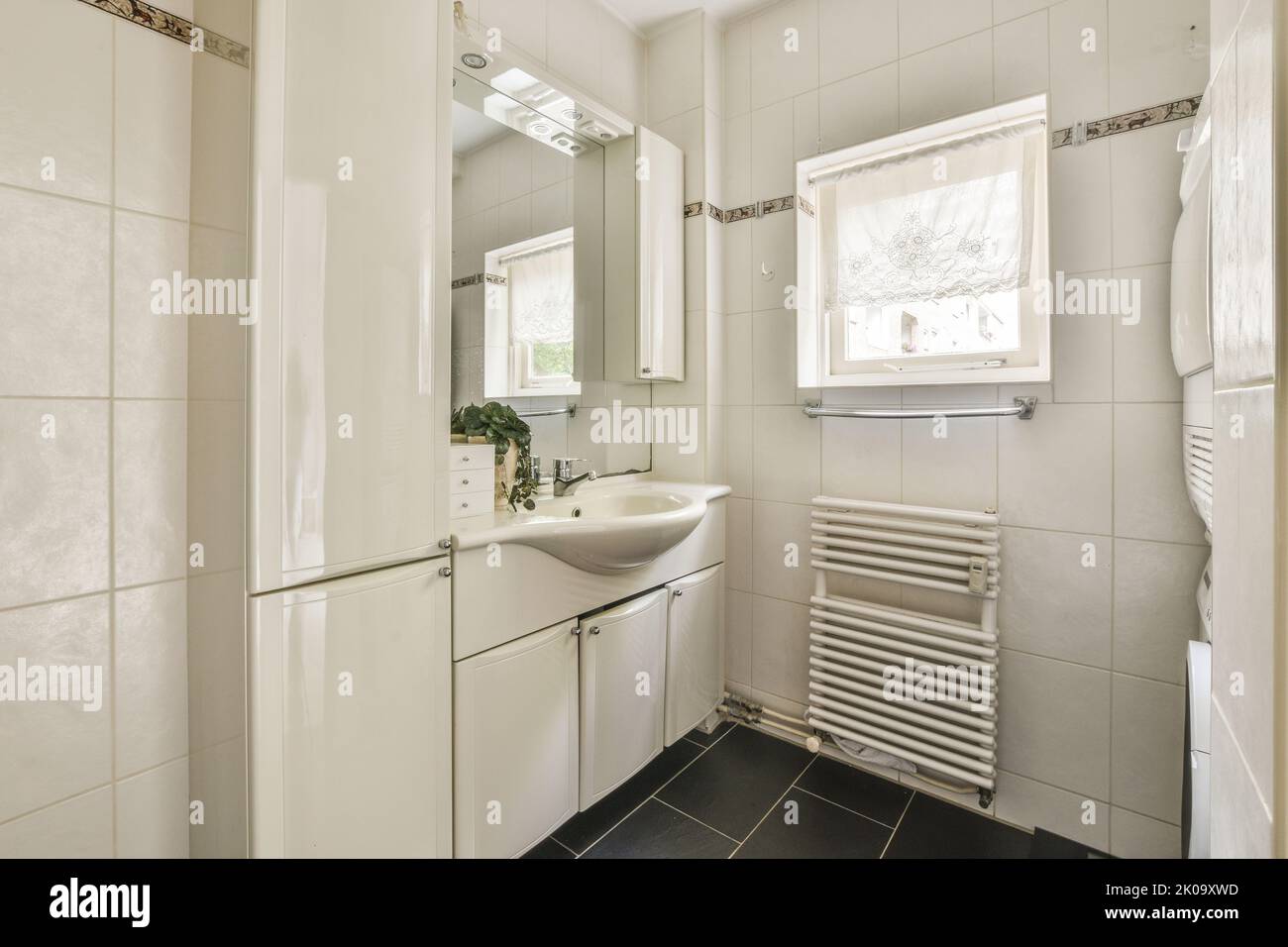 Flush toilet located between sink and shower in small tiled bathroom of