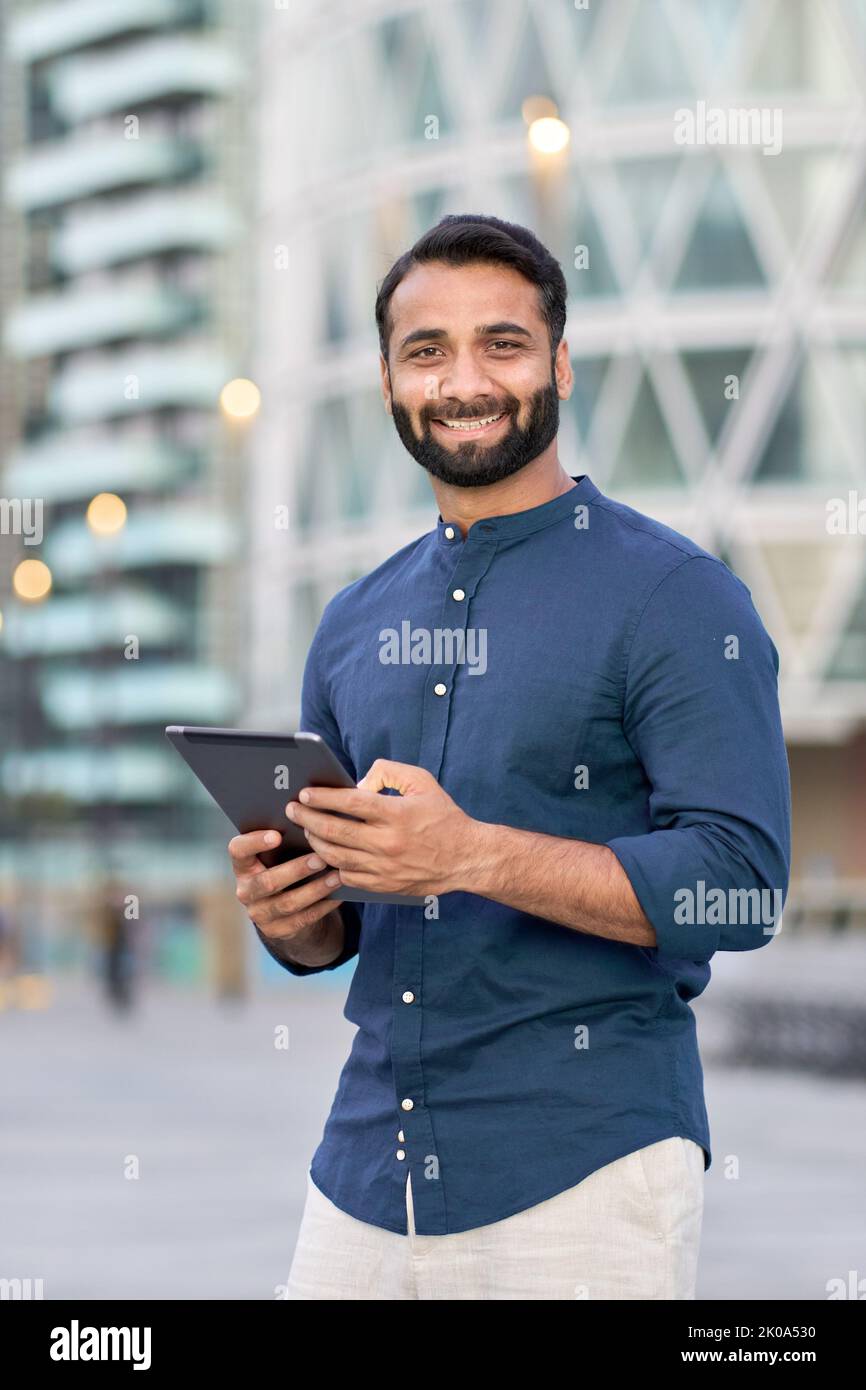 Smiling indian business man executive using digital tablet outdoors, vertical. Stock Photo