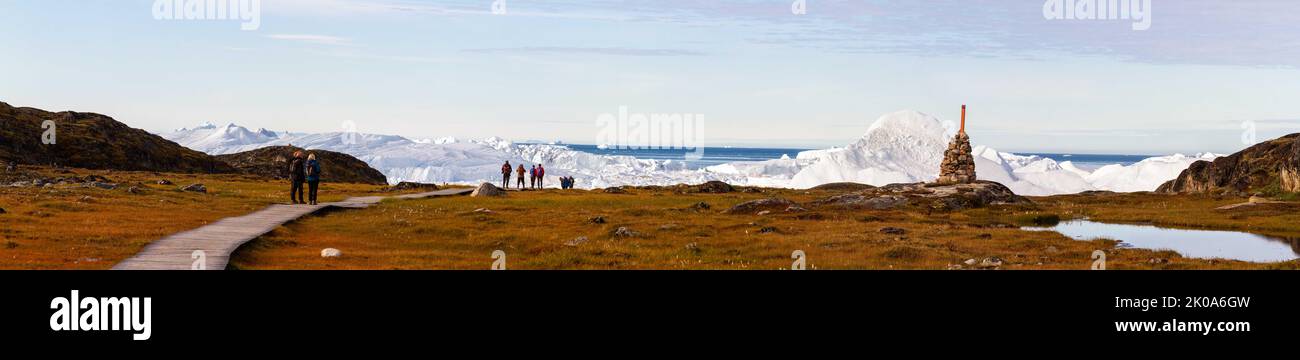 Ilulissat, Greenland - August 27, 2022 :  Tourists on boardwalk next to rock cairn at Ilulissat Icefiord, Greenland. , a Unesco World Heritage Site. Stock Photo
