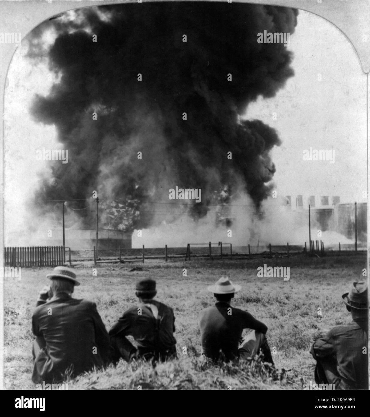 Burning for three days. Photographic print on stereo card view of four men seated on ground in foreground, watching oil well burning in the background Stock Photo