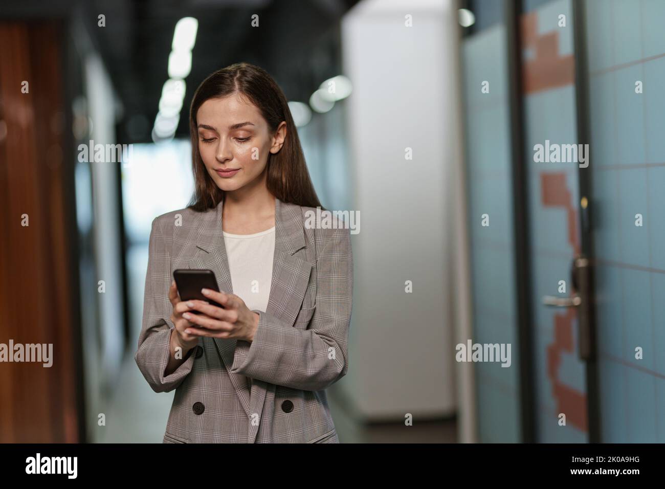 Portrait of attractive smiling business woman with mobile phone standing in modern coworking Stock Photo