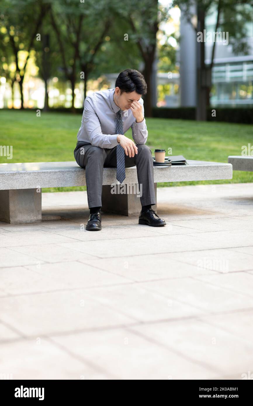 Tired young Chinese businessman sitting outdoors Stock Photo