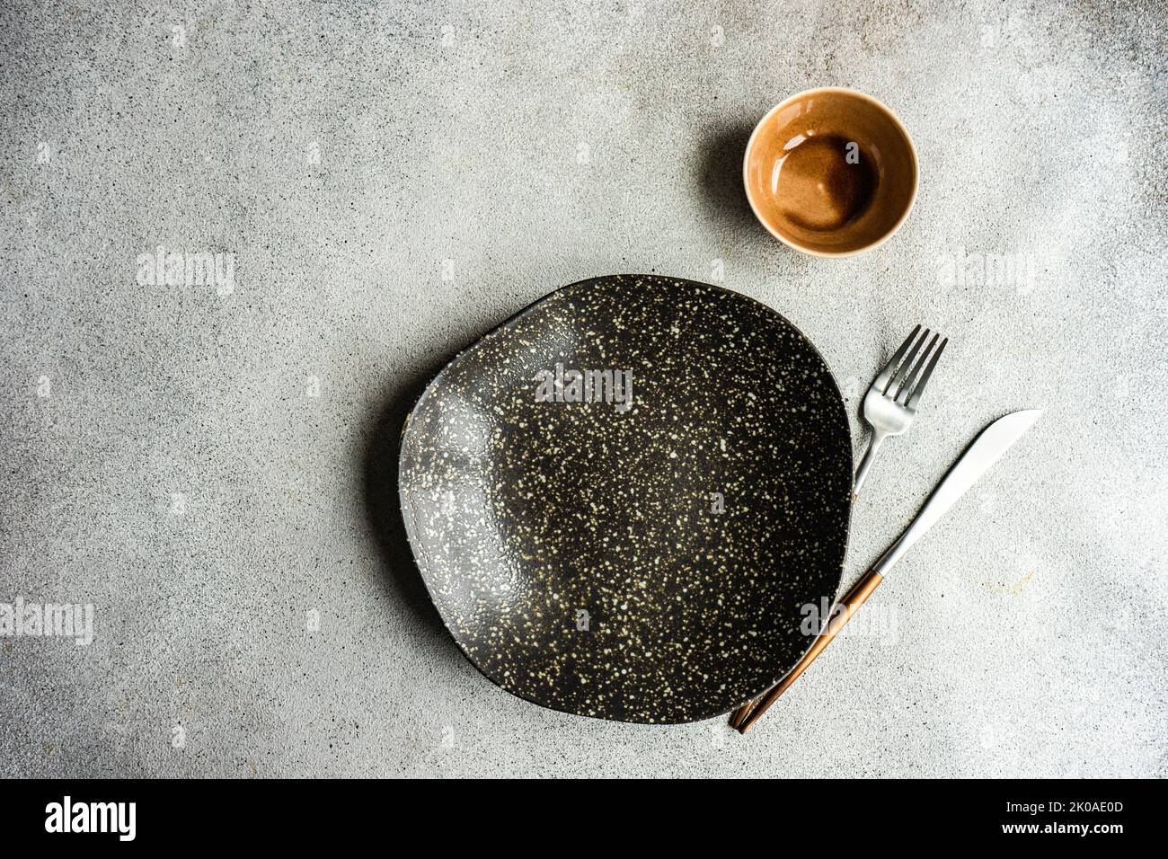 Minimalistic table setting with ceramic bowl and cutlery on concrete table Stock Photo
