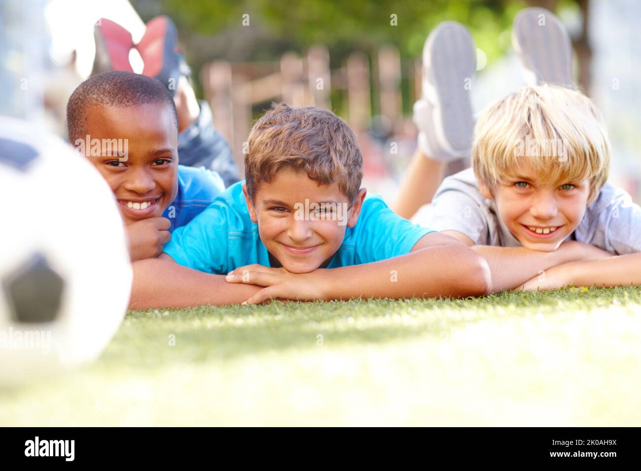 Having a ball at break-time. Three sweet boys lying on grass with a soccerball in the foreground - copyspace. Stock Photo