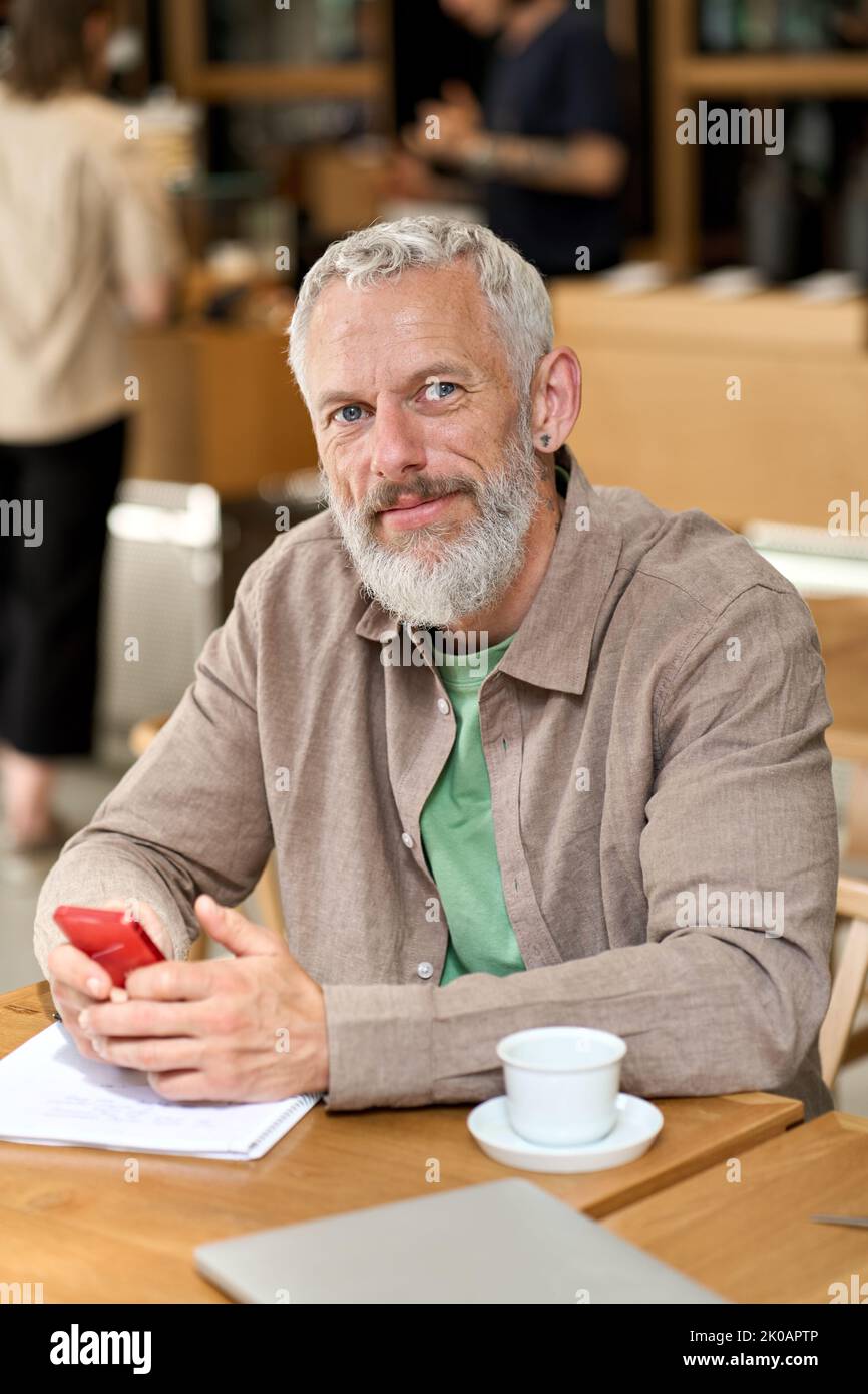 Middle aged business man using smartphone sitting at cafe table. Vertical Stock Photo