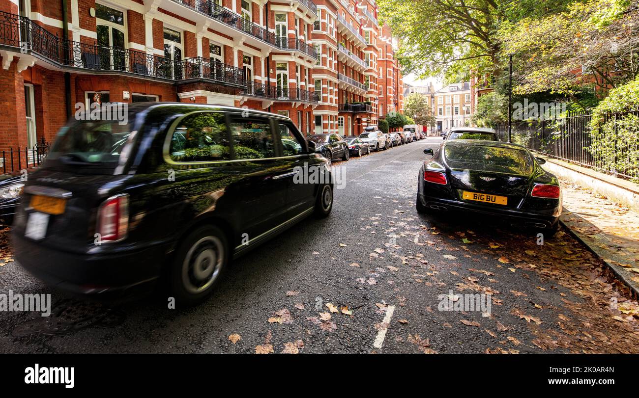 Speeding black London cab/taxi driving down Barkston Gardens, Kensington, London, past a black Aston Martin Stock Photo
