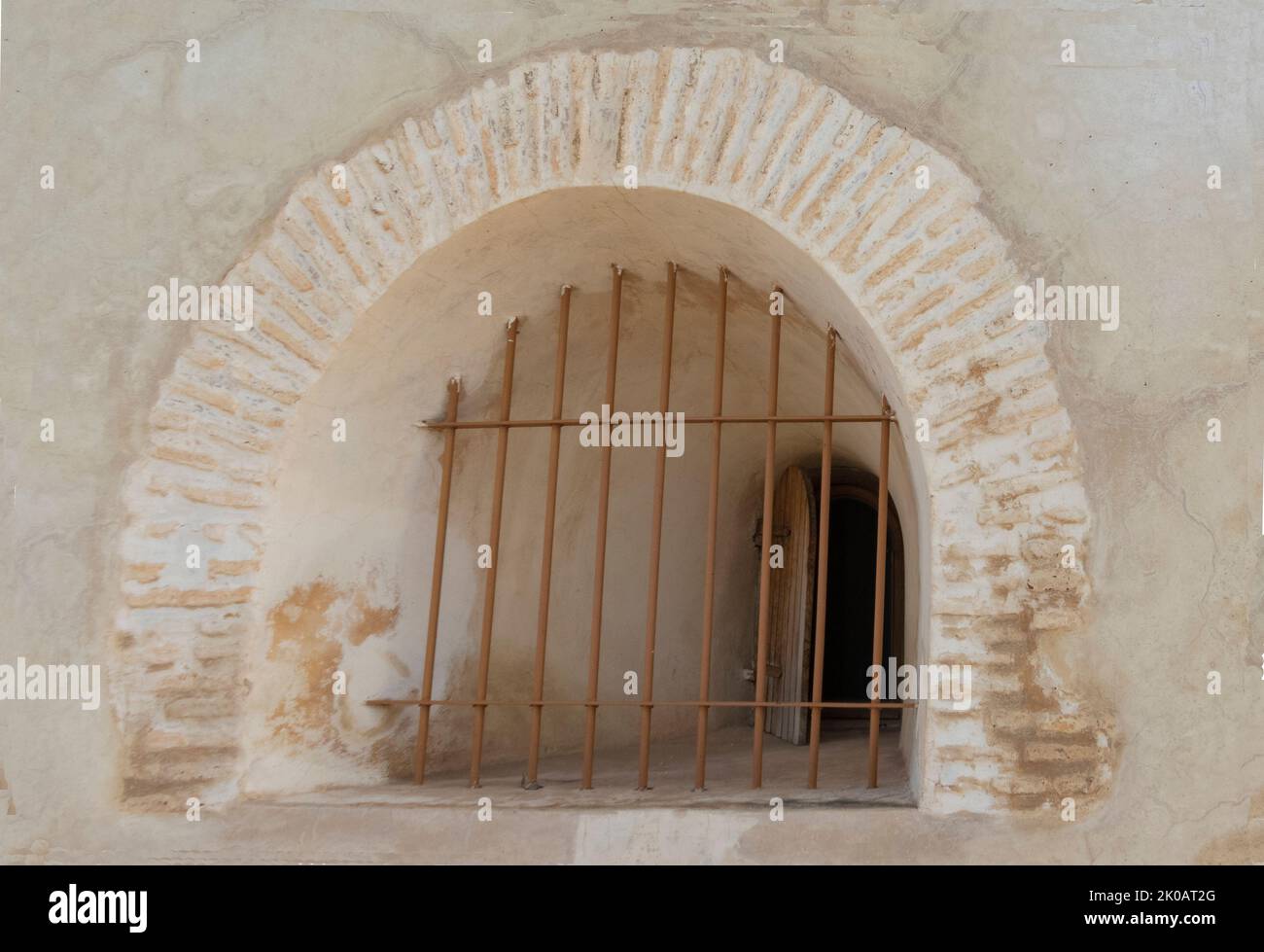 Curved window of pale stone in a wall in Morocco with iron bars painted white Stock Photo