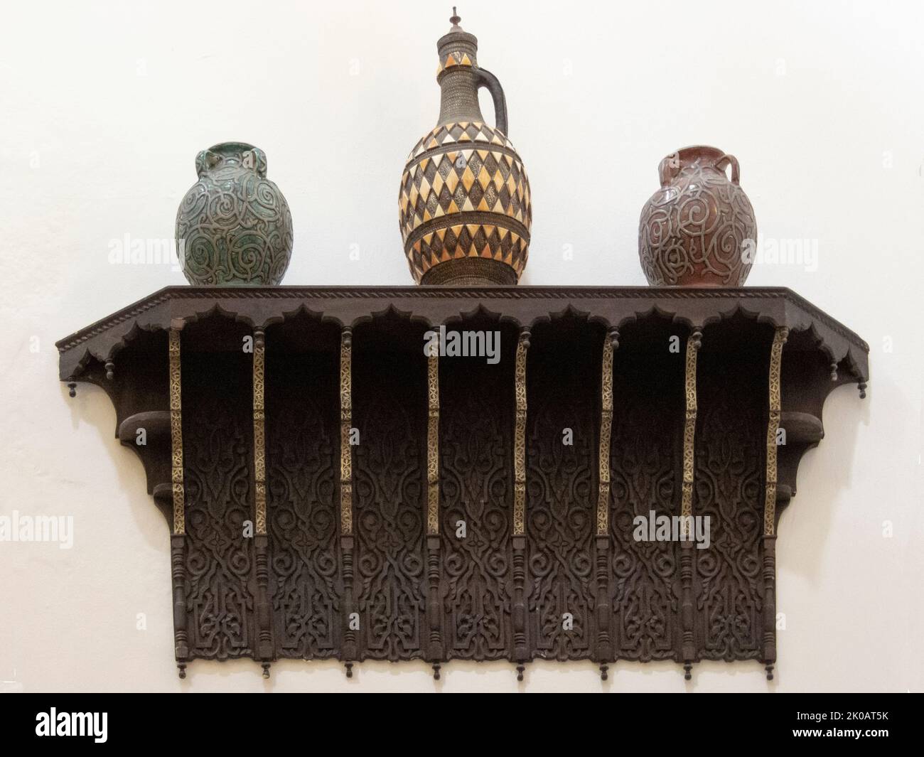 Three ceramic vases on a carved wooden shelf against a white wall Stock