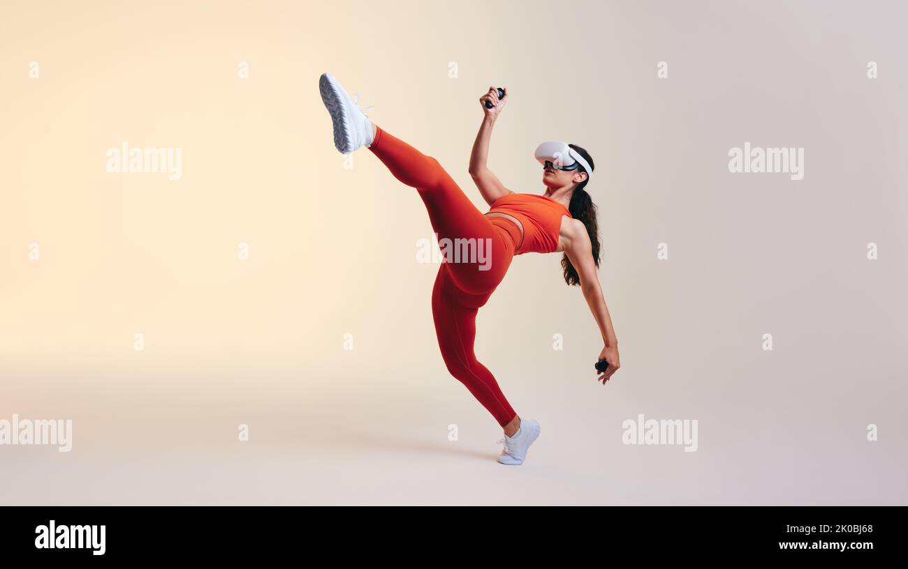 Sporty young woman working out using 3D technology. Athletic young woman exploring a virtual reality fitness game. Energetic young woman wearing virtu Stock Photo