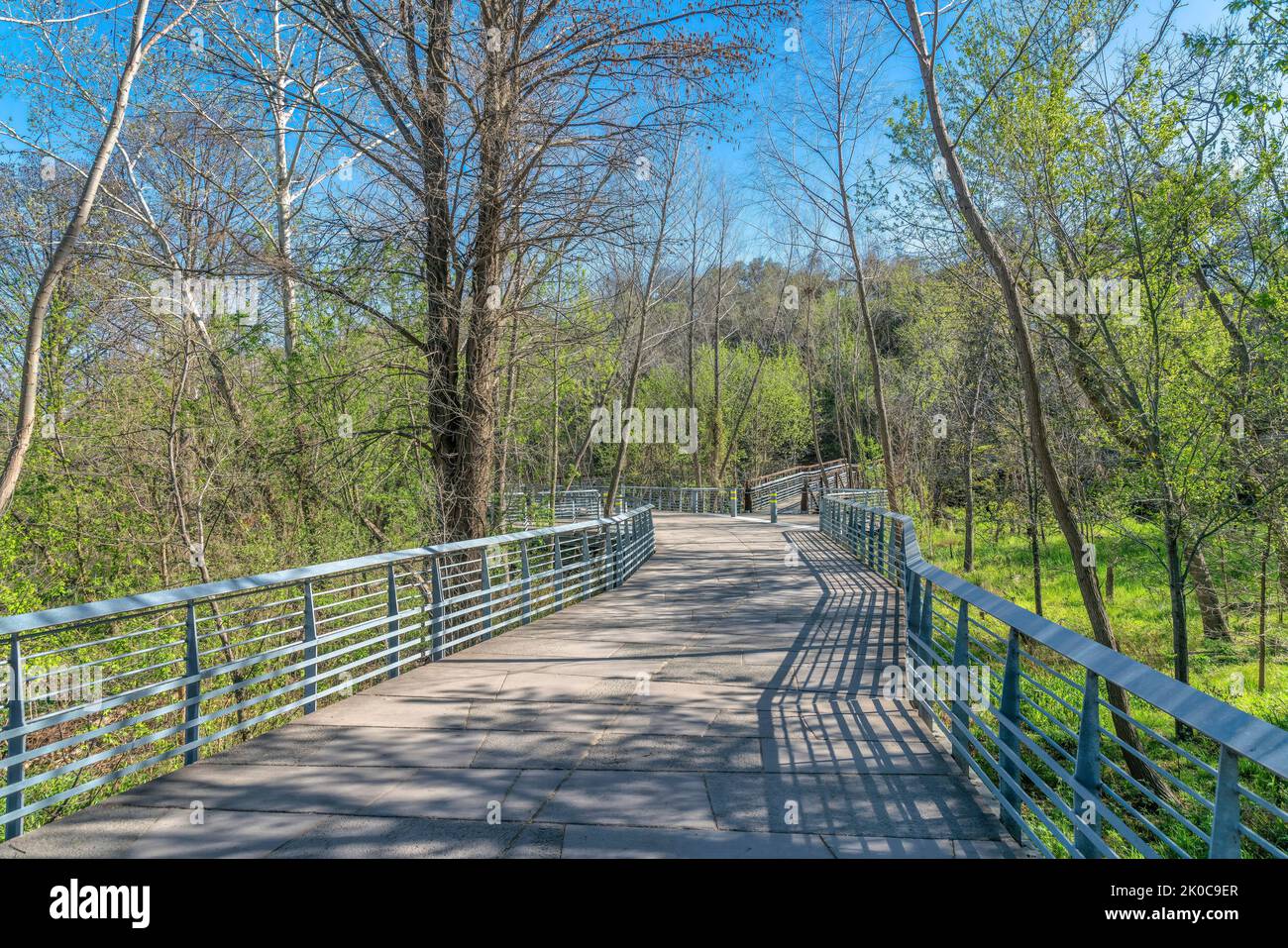 Austin, Texas- Concrete bike path and pedestrian pathway with railings over the grassland with trees. Boardwalk with metal railings in the middle of w Stock Photo