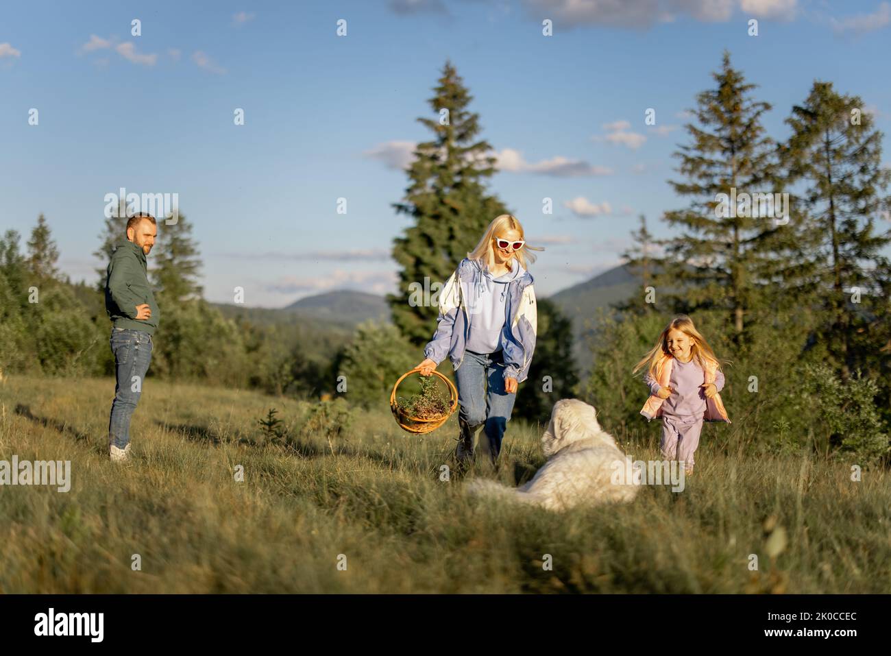 Young caucasian couple with little girl and dog have fun spending leisure time together on nature. Happy family traveling in the mountains Stock Photo