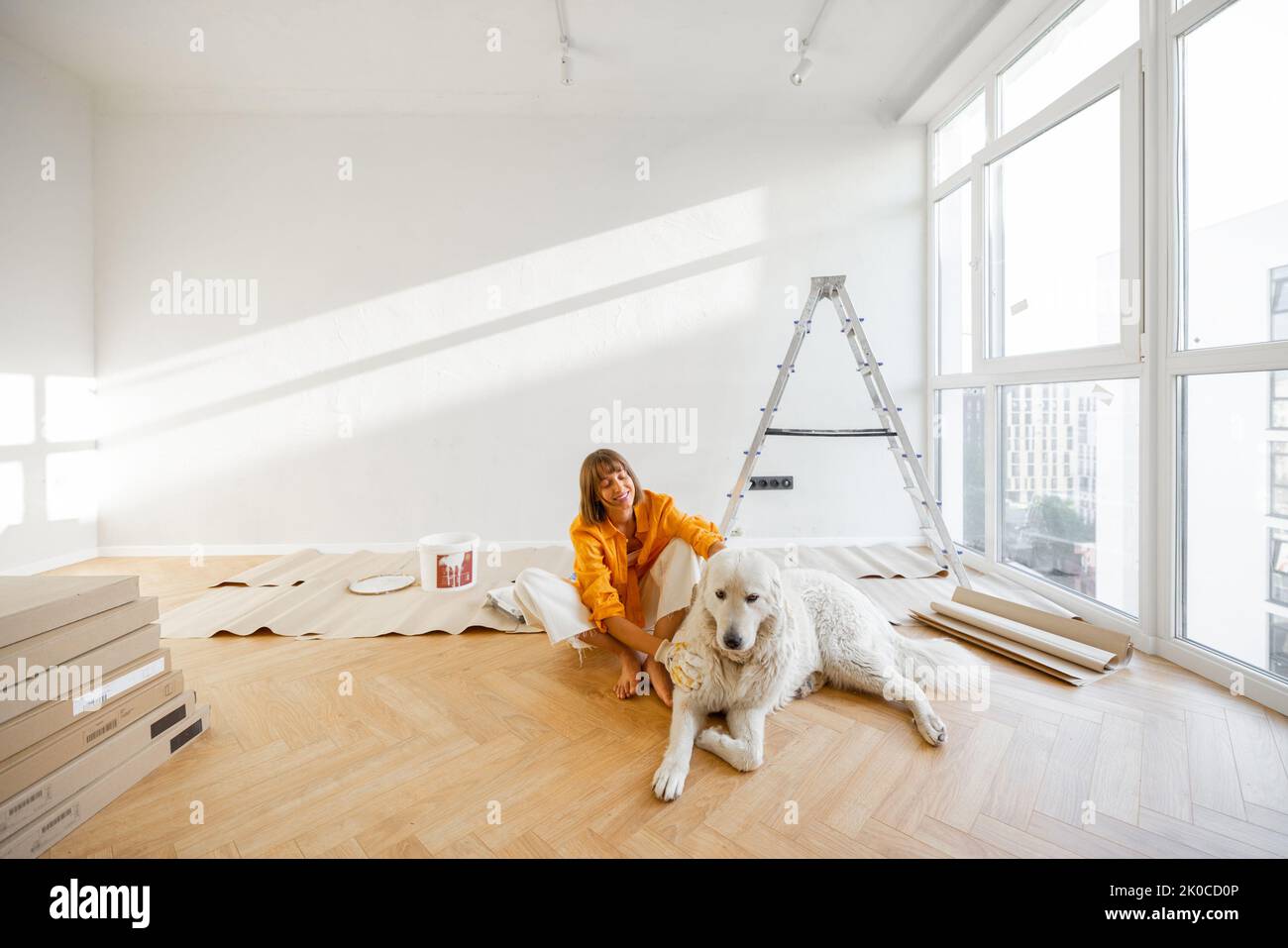 Young woman sits with her dog in room while making repairment in apartment. Repair and house renovation concept, friendship with pet Stock Photo