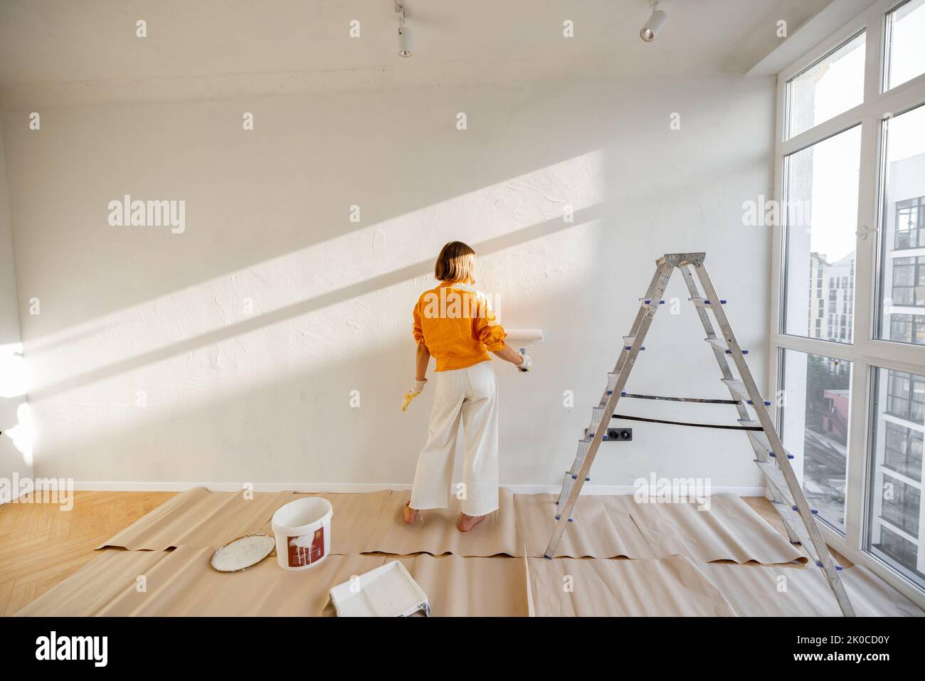 Woman paints the wall in white color while making repairment in newly purchased apartment. Repair and house renovation concept Stock Photo