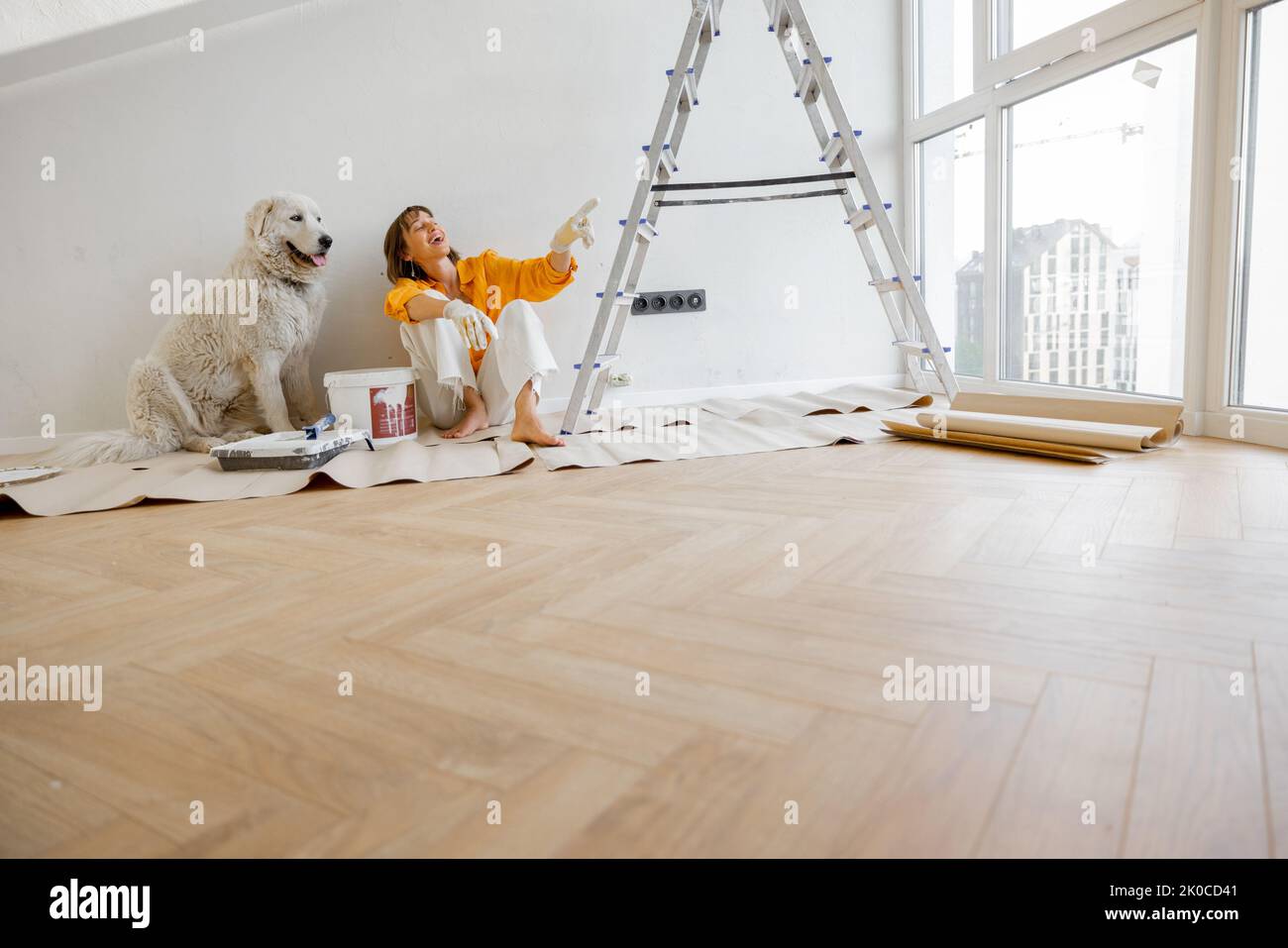Young woman sits with her dog in room while making repairing in apartment. Repair and house renovation concept, friendship with pet Stock Photo
