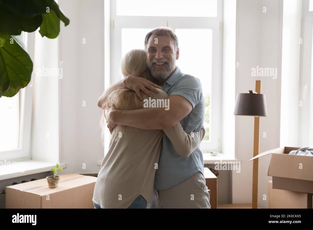 Happy retired grey haired couple hugging among moving boxes indoors Stock Photo