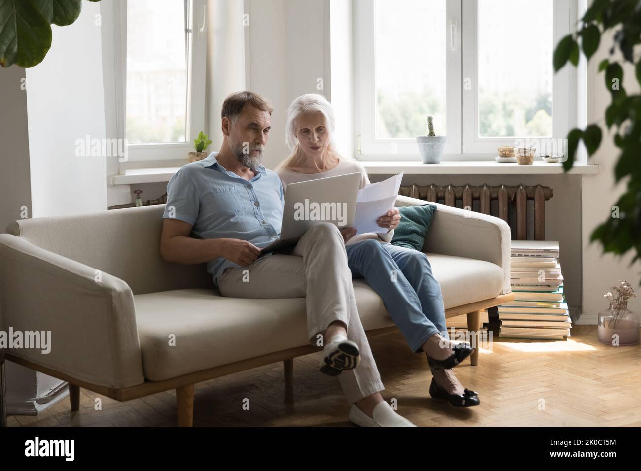 Serious older 60s couple paying paper bills on Internet Stock Photo
