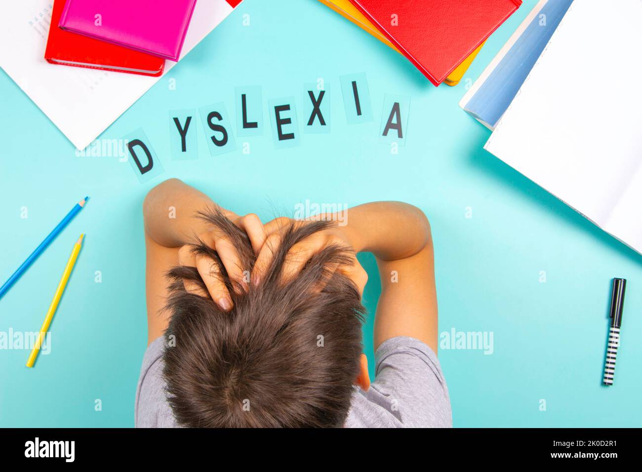 Sad tired frustrated teenage boy sitting at table with many books and