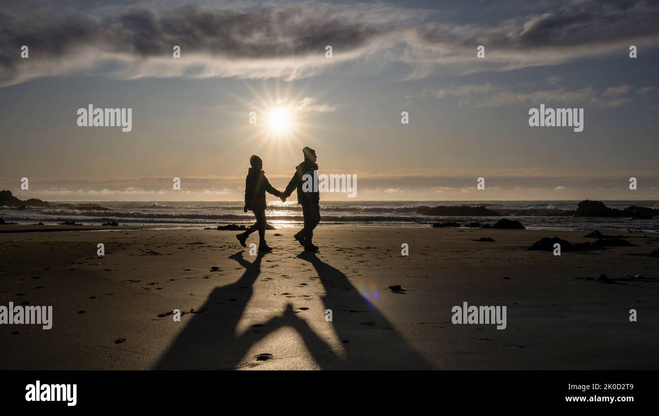 Couple holding hands, walking on the beach at sunrise.  Catlins, South Island. Stock Photo