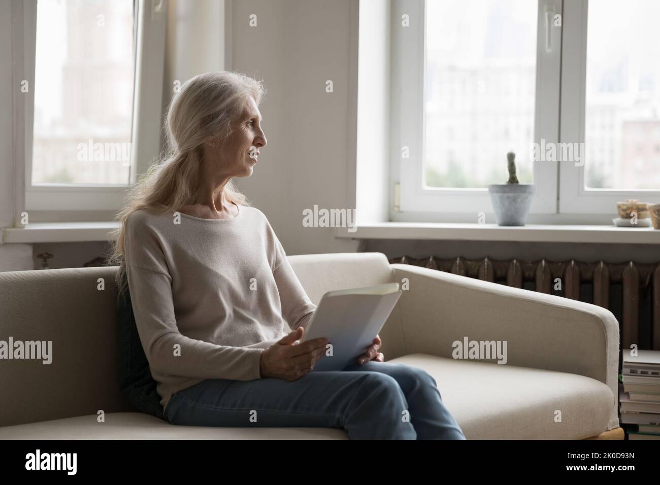 Positive thoughtful senior 70s lady holding tablet computer Stock Photo