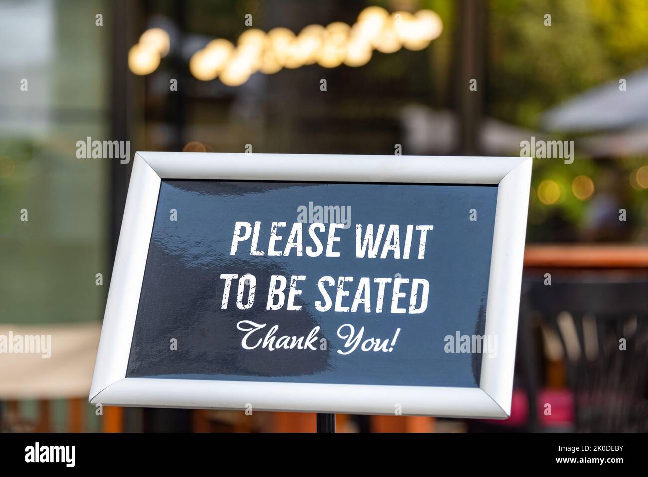 Please wait to be seated sign standing at the front of a restaurant. Sidewalk cafe hostess stand with message signboard for clients Stock Photo