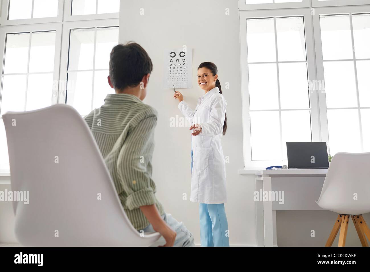 Ophthalmologist testing vision of little child and pointing at eye chart on wall Stock Photo