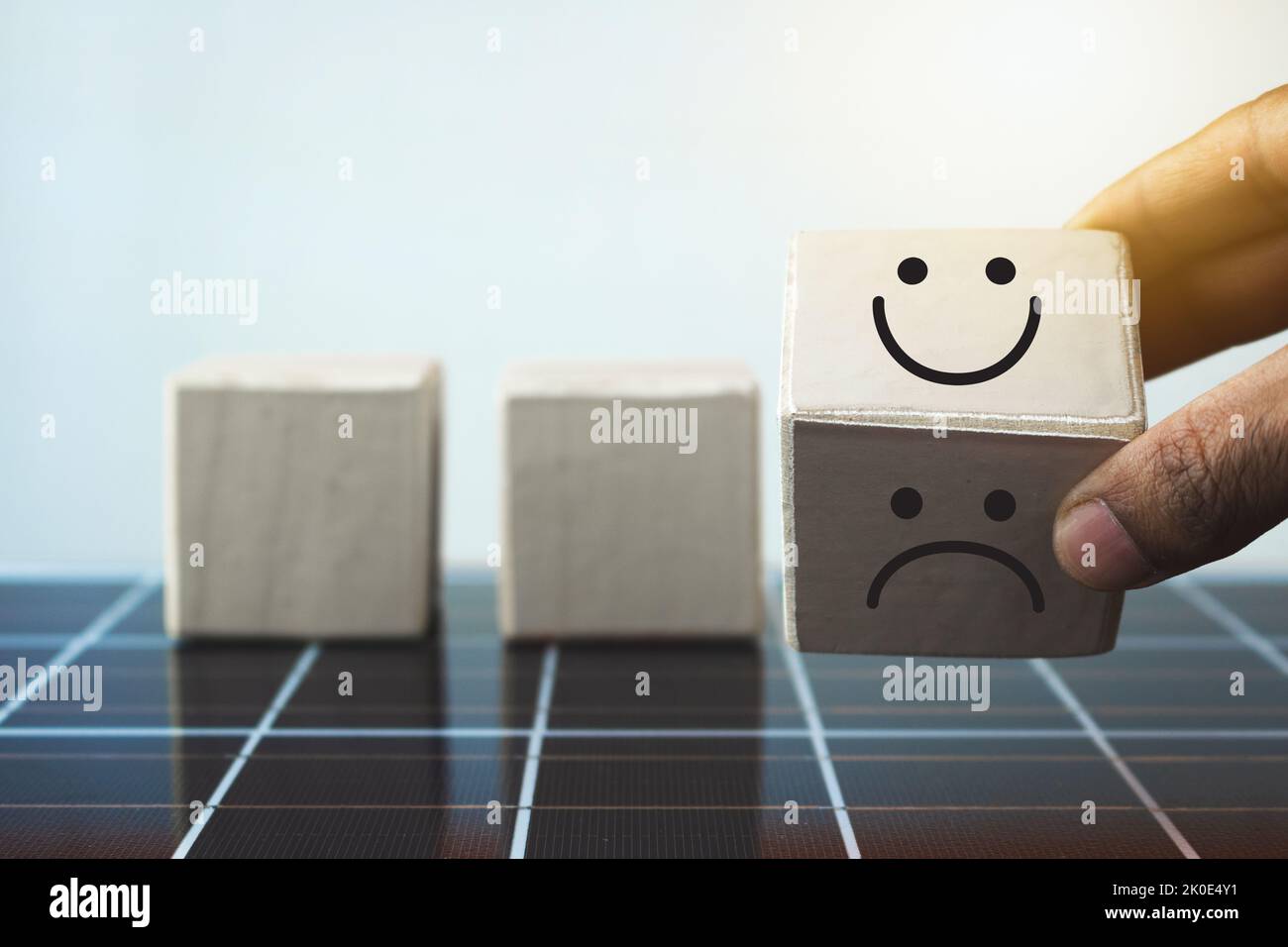 Hand puts wooden cubes with smile face in bright side and sad face in dark on photovoltaic solar panel. Stock Photo