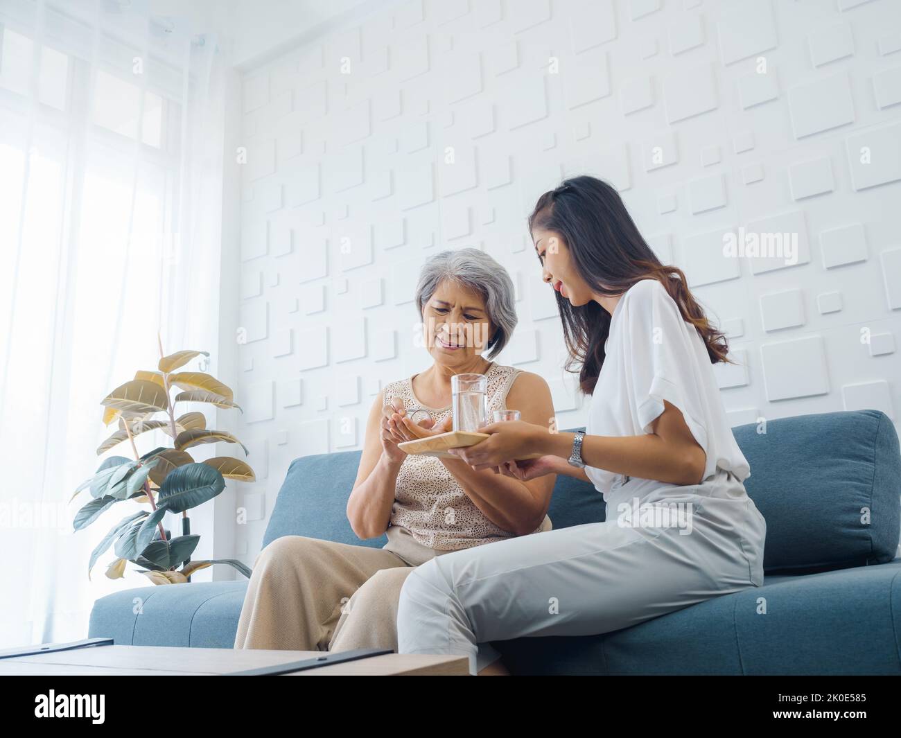 Portrait of Asian senior woman grey short hair holds pill and a glass of drinking water from young adult daughter, taken daily medicine or vitamin sup Stock Photo