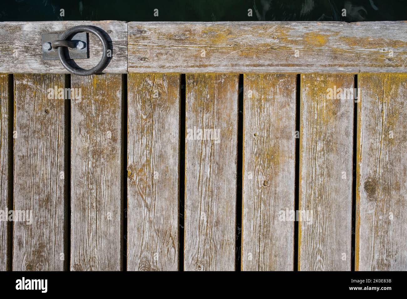 Old weathered wooden pier made of boards with a metal mooring ring. Copy space. Top view.  Stock Photo