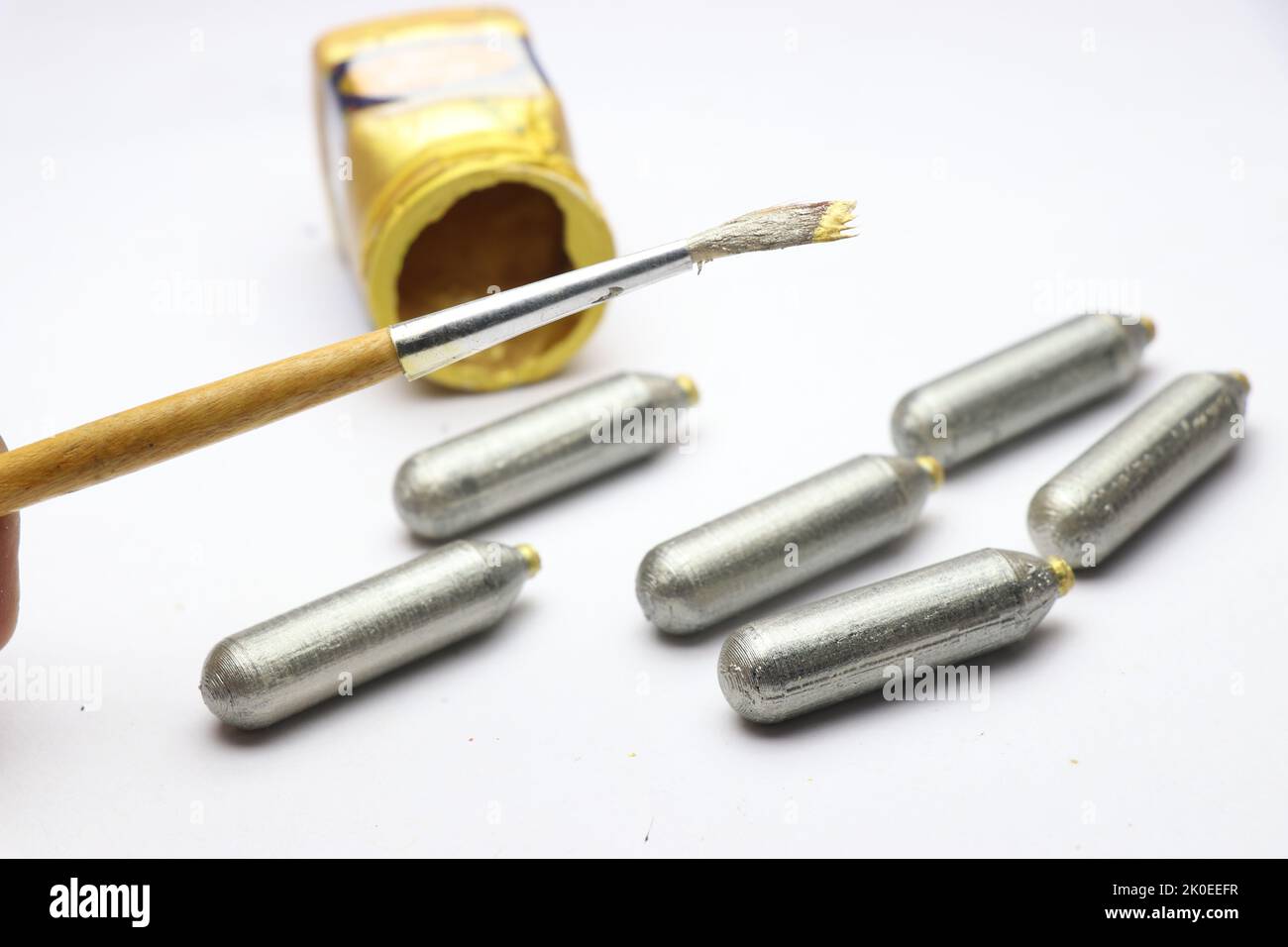Art and crafts work being done using a paint brush and silver color paint on some cylindrical shape object Stock Photo