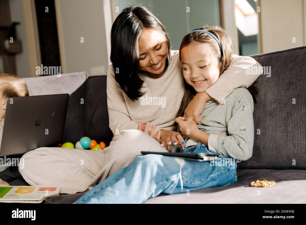 Happy mother using tablet computer while hugging her daughter at home Stock Photo