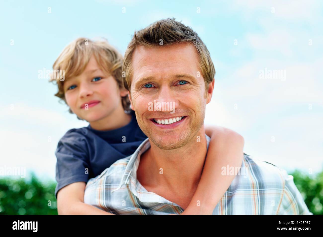 Smiling mature man piggybacking his son against sky. Portrait of a smiling mature man piggybacking his son against sky. Stock Photo