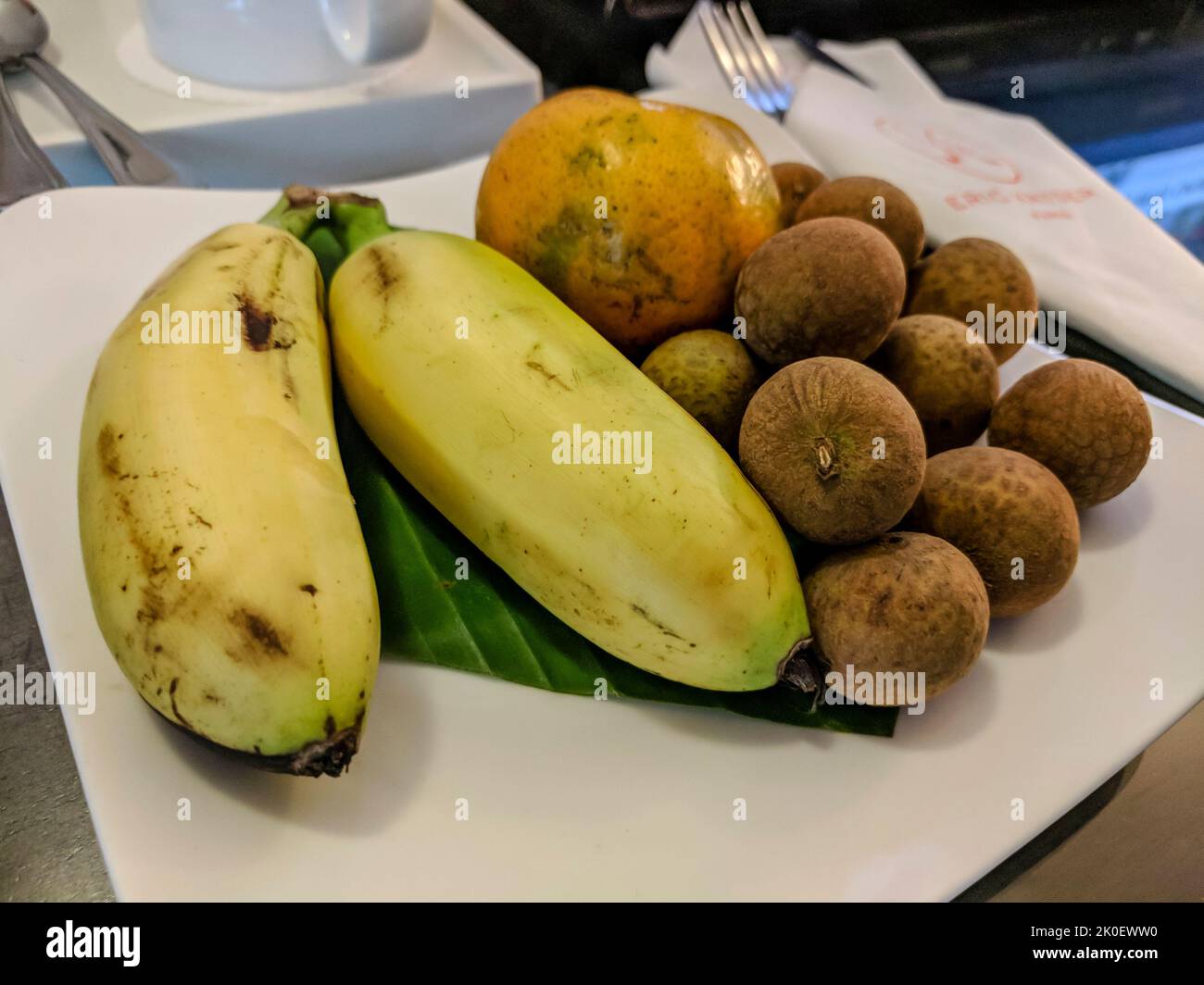 Plate with bananas, longan fruit and an orange in a hotel in Ho Chi Mihn City, Vietnam Stock Photo