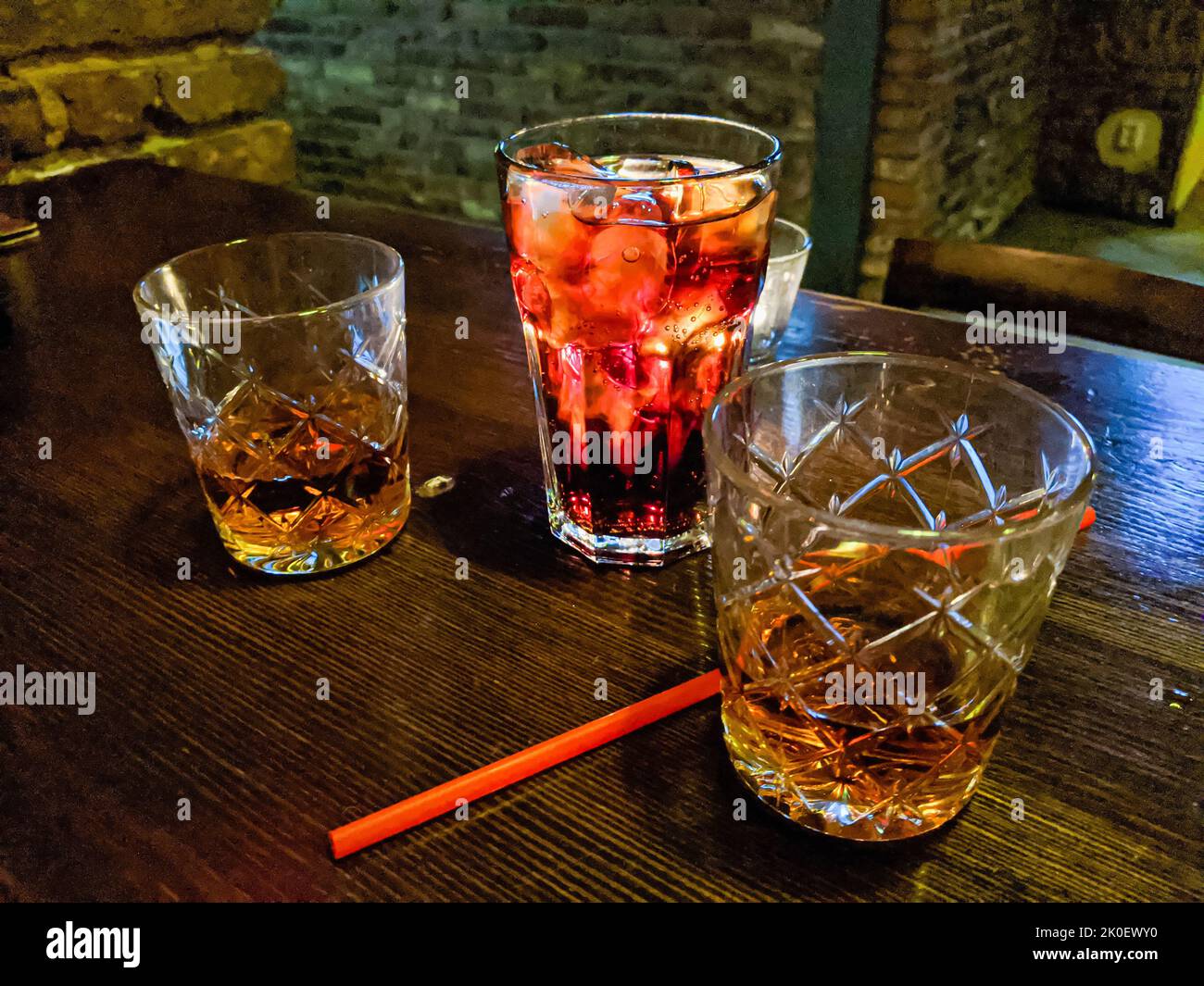 Two cut crystal glasses with rum, along with a glass containing cola on the table of a bar Stock Photo