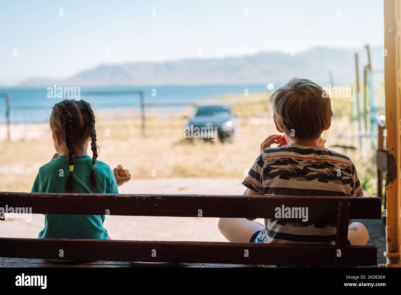 Children sitting on a bench eat watermelon in front of the sea Stock ...