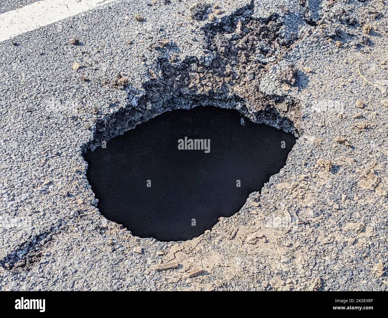 Deep sink hole opened up in a tarmac road surface. Stock Photo