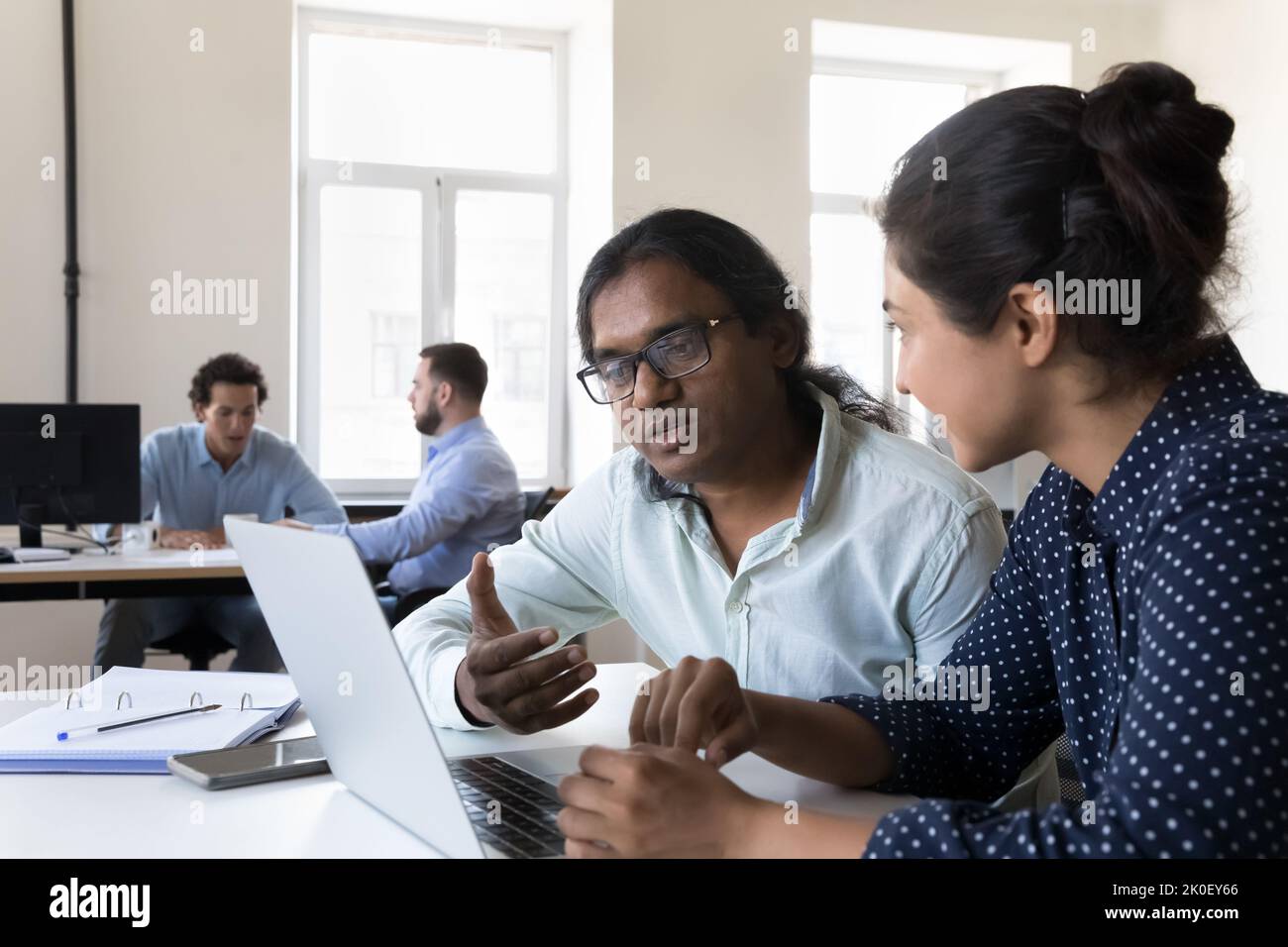 Two Indian employees collaborating on project, sitting at work table Stock Photo